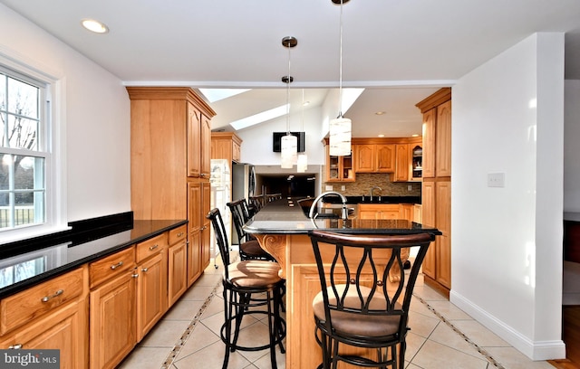 kitchen with light tile patterned flooring, decorative light fixtures, tasteful backsplash, sink, and a kitchen bar