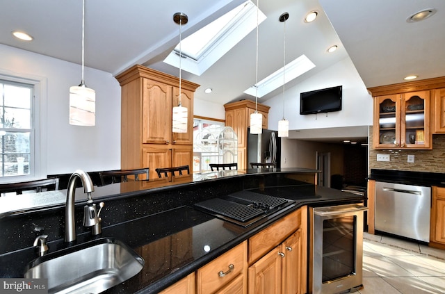 kitchen with appliances with stainless steel finishes, vaulted ceiling with skylight, pendant lighting, sink, and beverage cooler