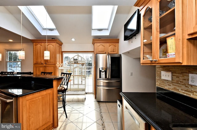 kitchen with pendant lighting, a breakfast bar area, dark stone countertops, stainless steel refrigerator with ice dispenser, and decorative backsplash