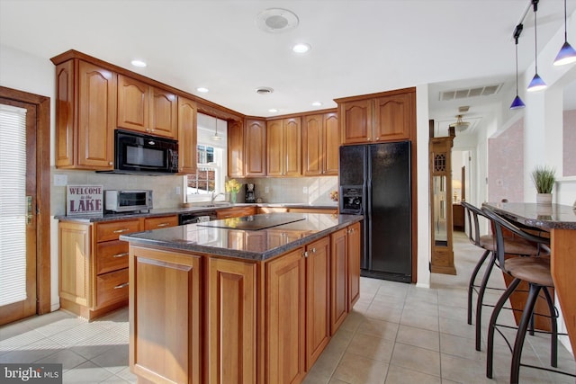 kitchen featuring light tile patterned flooring, a kitchen island, backsplash, hanging light fixtures, and black appliances