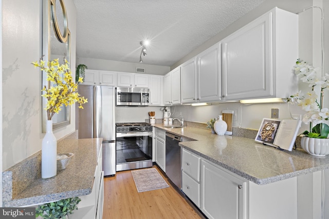 kitchen featuring appliances with stainless steel finishes, white cabinets, light hardwood / wood-style floors, kitchen peninsula, and a textured ceiling