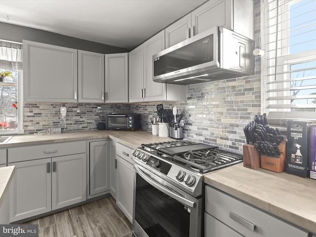 kitchen with a healthy amount of sunlight, stainless steel appliances, gray cabinets, and decorative backsplash