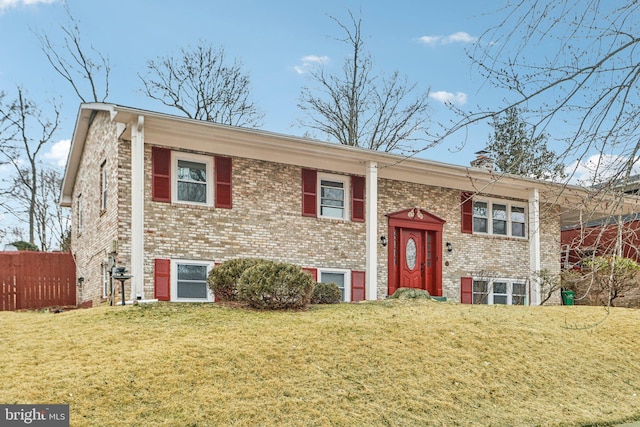 raised ranch with fence, a front lawn, and brick siding