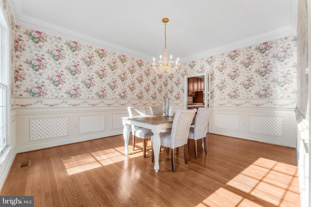 dining area with wainscoting, wood finished floors, an inviting chandelier, and wallpapered walls