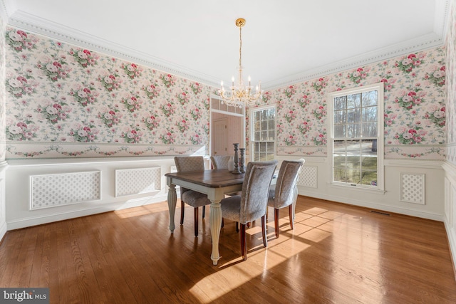 dining space featuring wallpapered walls, a notable chandelier, a wainscoted wall, and wood finished floors