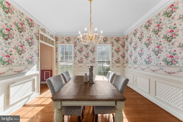 dining area with wood finished floors, ornamental molding, wainscoting, wallpapered walls, and an inviting chandelier