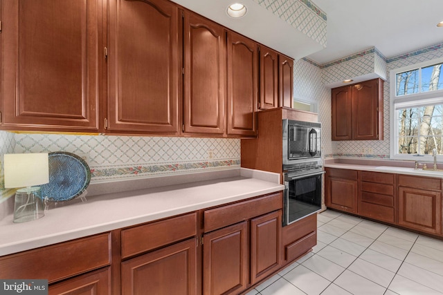 kitchen with brown cabinets, light countertops, black appliances, and wallpapered walls