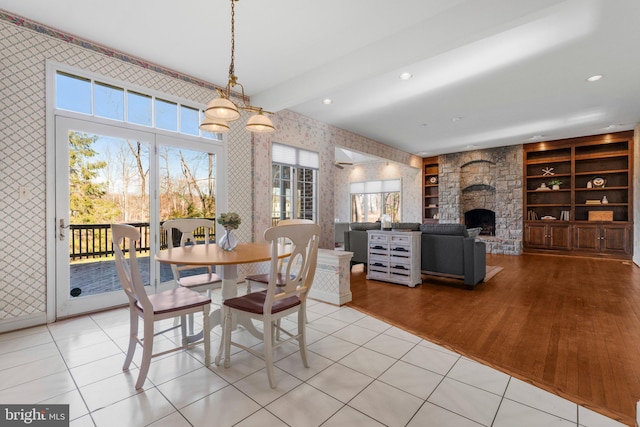 dining space with light wood-type flooring, a stone fireplace, recessed lighting, and wallpapered walls