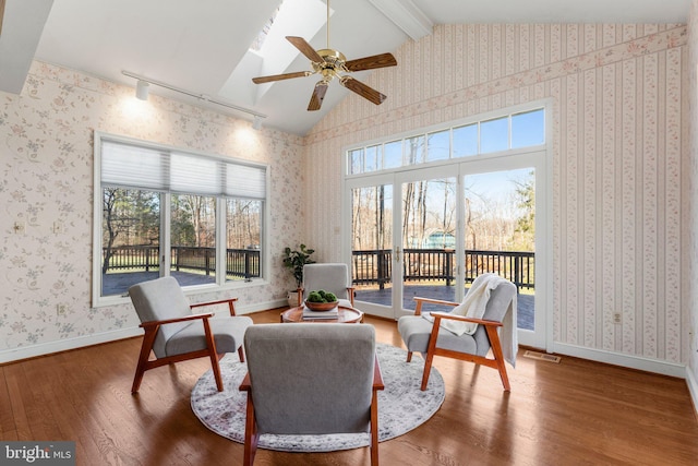 sitting room featuring lofted ceiling with beams, ceiling fan, wood finished floors, baseboards, and wallpapered walls