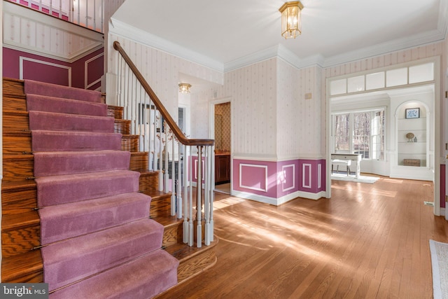 staircase featuring wallpapered walls, ornamental molding, wood finished floors, and wainscoting