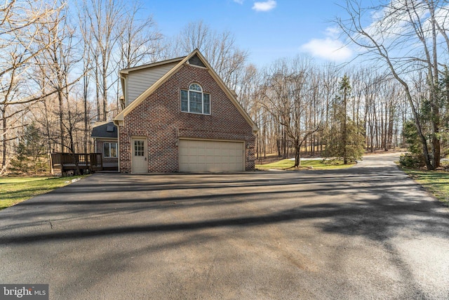 view of side of home with a garage, a deck, aphalt driveway, and brick siding