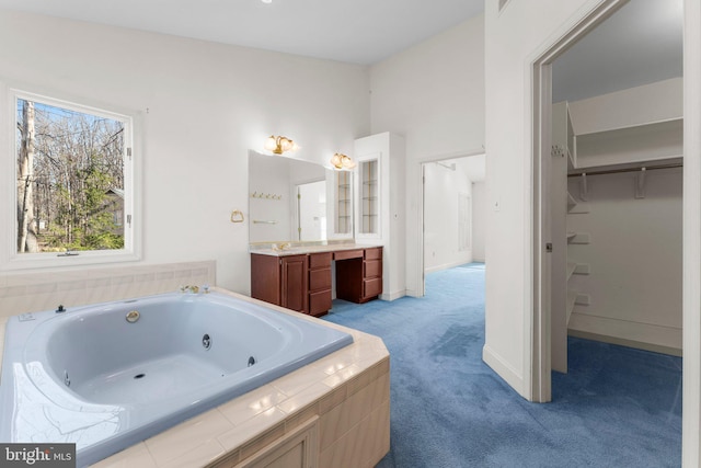 full bath featuring baseboards, a spacious closet, a tub with jets, and vanity