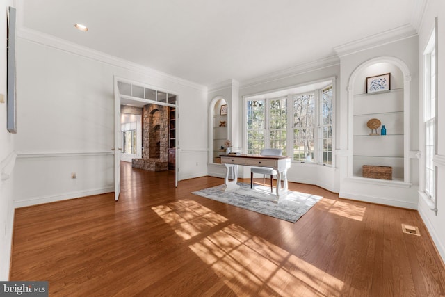 interior space featuring visible vents, built in features, crown molding, and wood finished floors