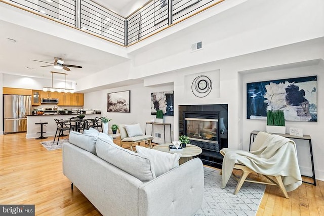 living room featuring light hardwood / wood-style floors, ceiling fan, and a high ceiling