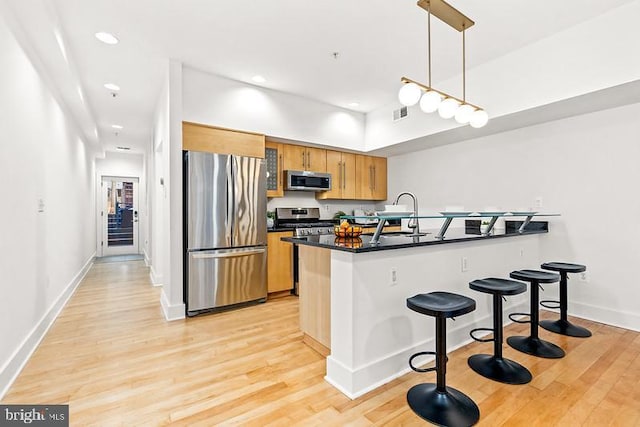 kitchen with appliances with stainless steel finishes, sink, hanging light fixtures, kitchen peninsula, and light wood-type flooring