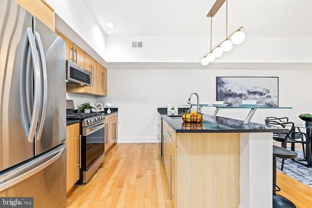 kitchen with pendant lighting, sink, light hardwood / wood-style flooring, stainless steel appliances, and a kitchen breakfast bar