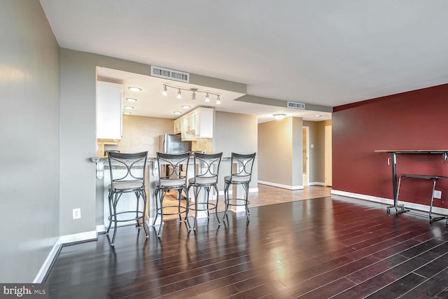 kitchen with a breakfast bar, dark hardwood / wood-style floors, stainless steel fridge, kitchen peninsula, and white cabinets