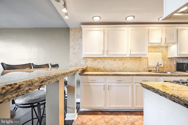 kitchen featuring tasteful backsplash, white cabinetry, sink, a breakfast bar area, and light stone countertops