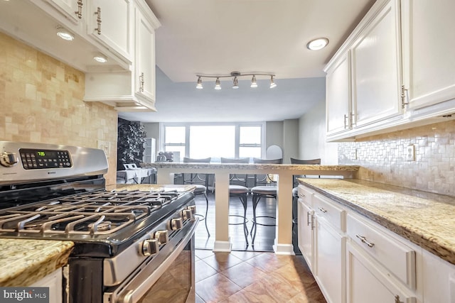 kitchen featuring stainless steel gas stove, white cabinetry, tasteful backsplash, light stone countertops, and dark tile patterned flooring