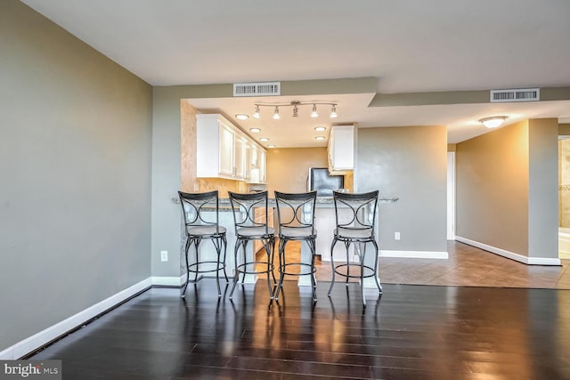 kitchen with white cabinetry, dark hardwood / wood-style flooring, a breakfast bar area, and stainless steel fridge