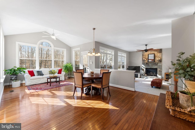 dining room with ceiling fan with notable chandelier, wood-type flooring, a fireplace, and vaulted ceiling