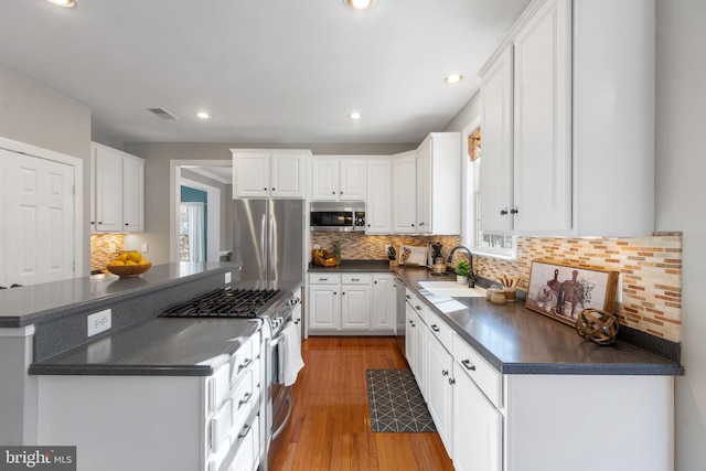 kitchen featuring sink, light hardwood / wood-style flooring, appliances with stainless steel finishes, tasteful backsplash, and white cabinets