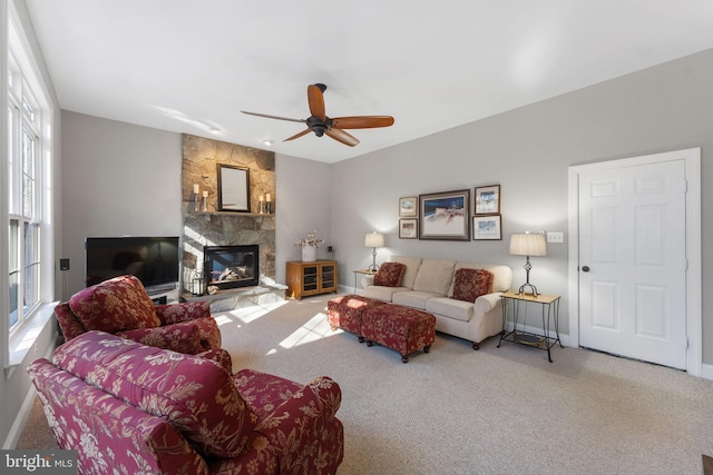 carpeted living room featuring ceiling fan and a stone fireplace