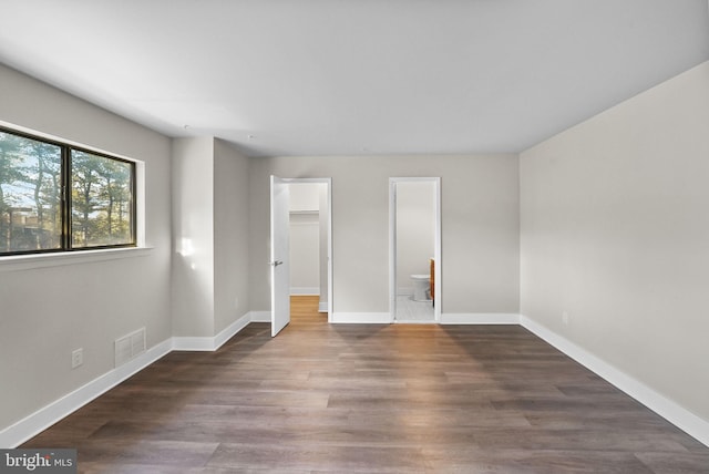 unfurnished bedroom featuring ensuite bathroom and dark hardwood / wood-style floors