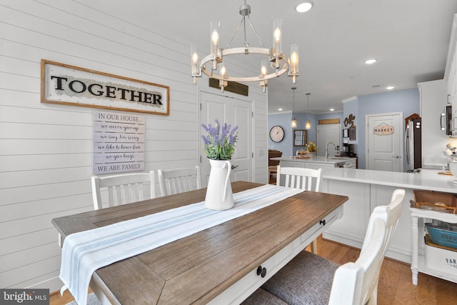 dining room featuring sink, hardwood / wood-style floors, an inviting chandelier, and wood walls