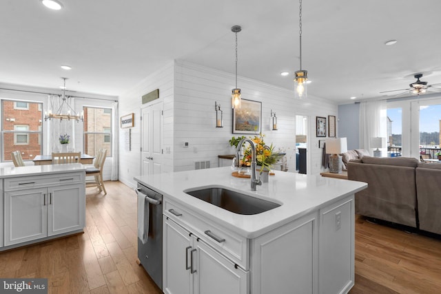 kitchen with pendant lighting, white cabinetry, sink, stainless steel dishwasher, and a center island with sink