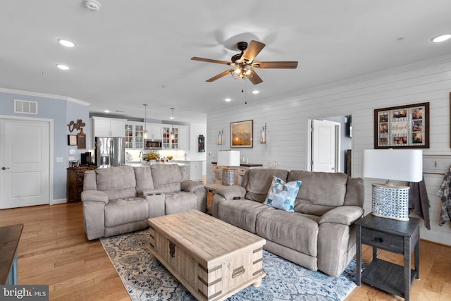 living room featuring light hardwood / wood-style flooring, ornamental molding, wooden walls, and ceiling fan