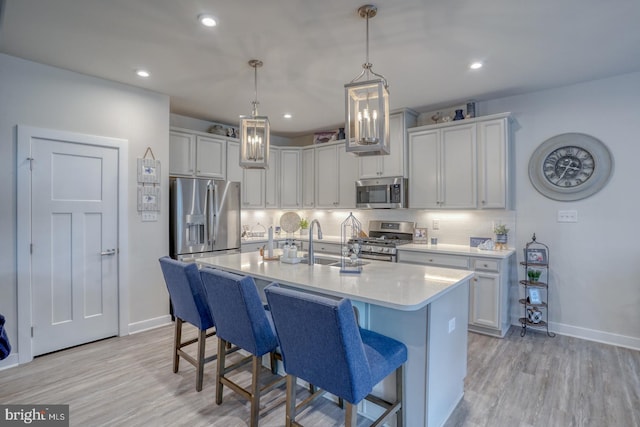 kitchen featuring sink, stainless steel appliances, decorative backsplash, decorative light fixtures, and light wood-type flooring