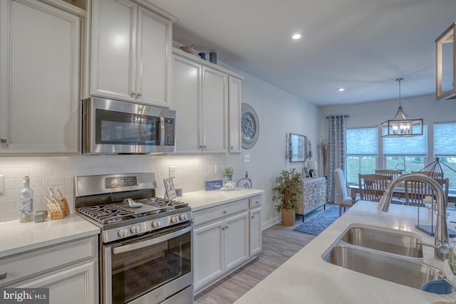 kitchen featuring sink, light hardwood / wood-style flooring, appliances with stainless steel finishes, a notable chandelier, and decorative backsplash