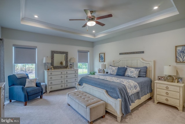 bedroom with multiple windows, light colored carpet, a raised ceiling, and ceiling fan