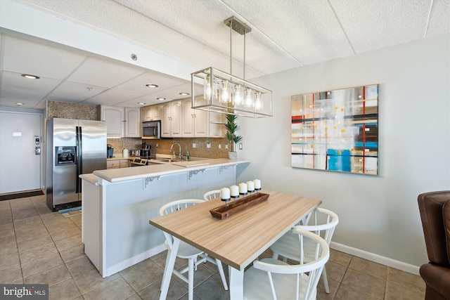 kitchen featuring decorative light fixtures, light tile patterned floors, appliances with stainless steel finishes, kitchen peninsula, and decorative backsplash