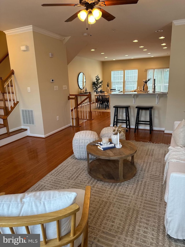 living room featuring dark wood-type flooring, ornamental molding, and ceiling fan