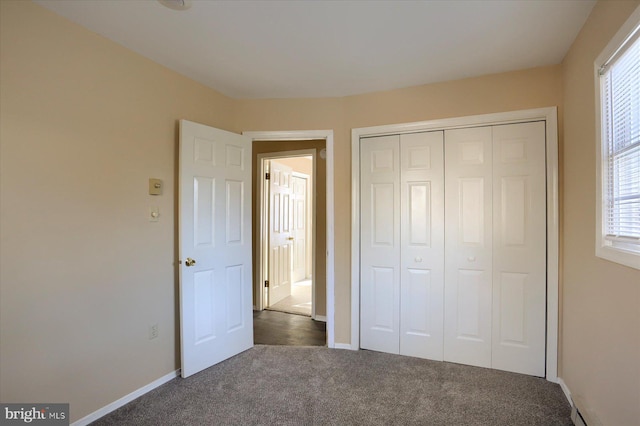 unfurnished bedroom featuring multiple windows, dark colored carpet, and a closet