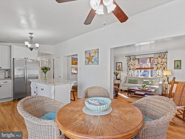 dining space with ceiling fan with notable chandelier and light wood-type flooring