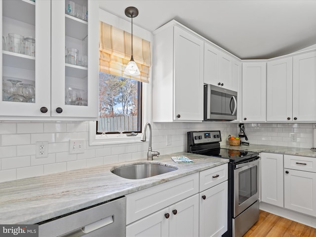 kitchen with appliances with stainless steel finishes, sink, white cabinets, hanging light fixtures, and light stone countertops