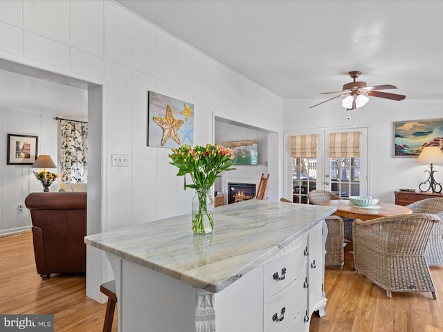 kitchen featuring a breakfast bar, light stone counters, light hardwood / wood-style flooring, ceiling fan, and white cabinets