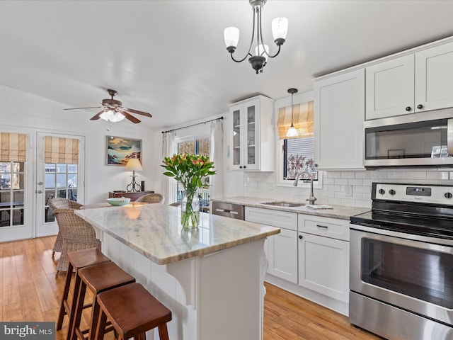 kitchen with a kitchen island, appliances with stainless steel finishes, pendant lighting, white cabinetry, and sink