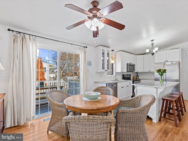 dining area with ceiling fan with notable chandelier, sink, and light wood-type flooring