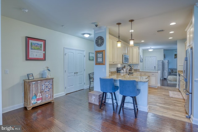 kitchen with pendant lighting, a breakfast bar area, appliances with stainless steel finishes, light stone countertops, and kitchen peninsula