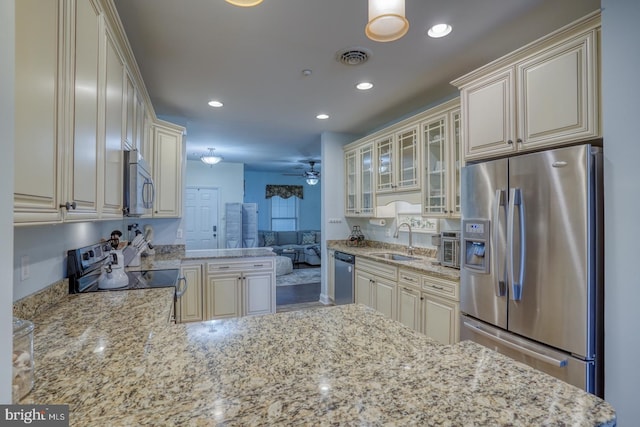 kitchen with sink, stainless steel appliances, cream cabinetry, and light stone countertops