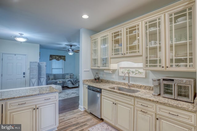 kitchen with sink, light stone counters, light hardwood / wood-style flooring, stainless steel dishwasher, and cream cabinetry