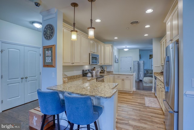 kitchen featuring a kitchen bar, decorative light fixtures, kitchen peninsula, stainless steel appliances, and light stone countertops