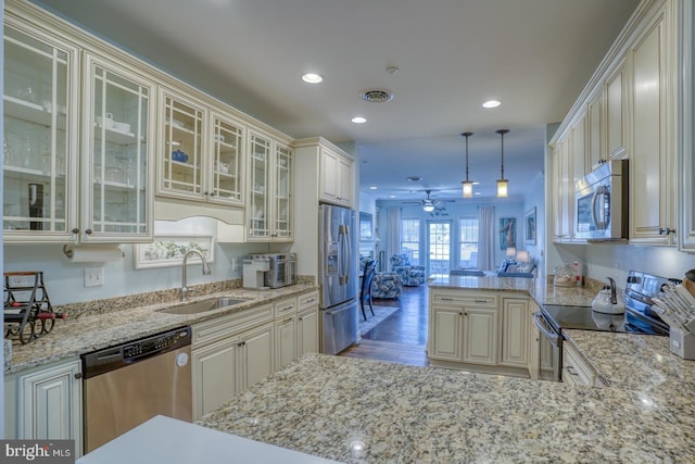 kitchen with light stone counters, hanging light fixtures, sink, and appliances with stainless steel finishes