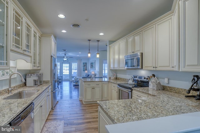 kitchen with sink, hanging light fixtures, stainless steel appliances, kitchen peninsula, and cream cabinetry