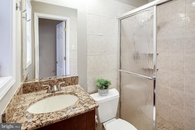 bathroom with vanity, toilet, a shower with door, and tile walls