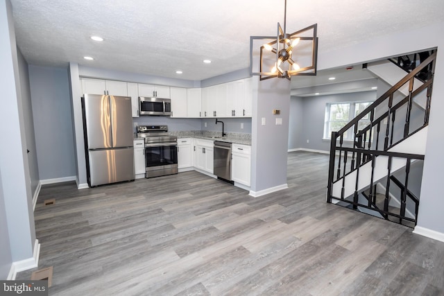 kitchen with baseboards, appliances with stainless steel finishes, a textured ceiling, light wood-style floors, and a sink